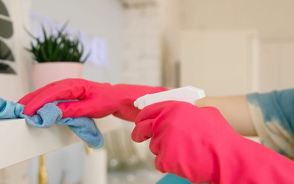 Hands in pink gloves cleaning a shelf