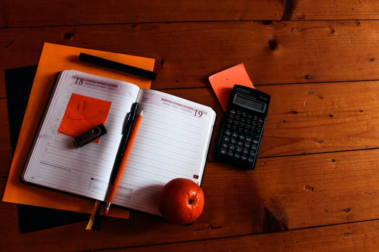 Calculator, orange, notebook, and a pen