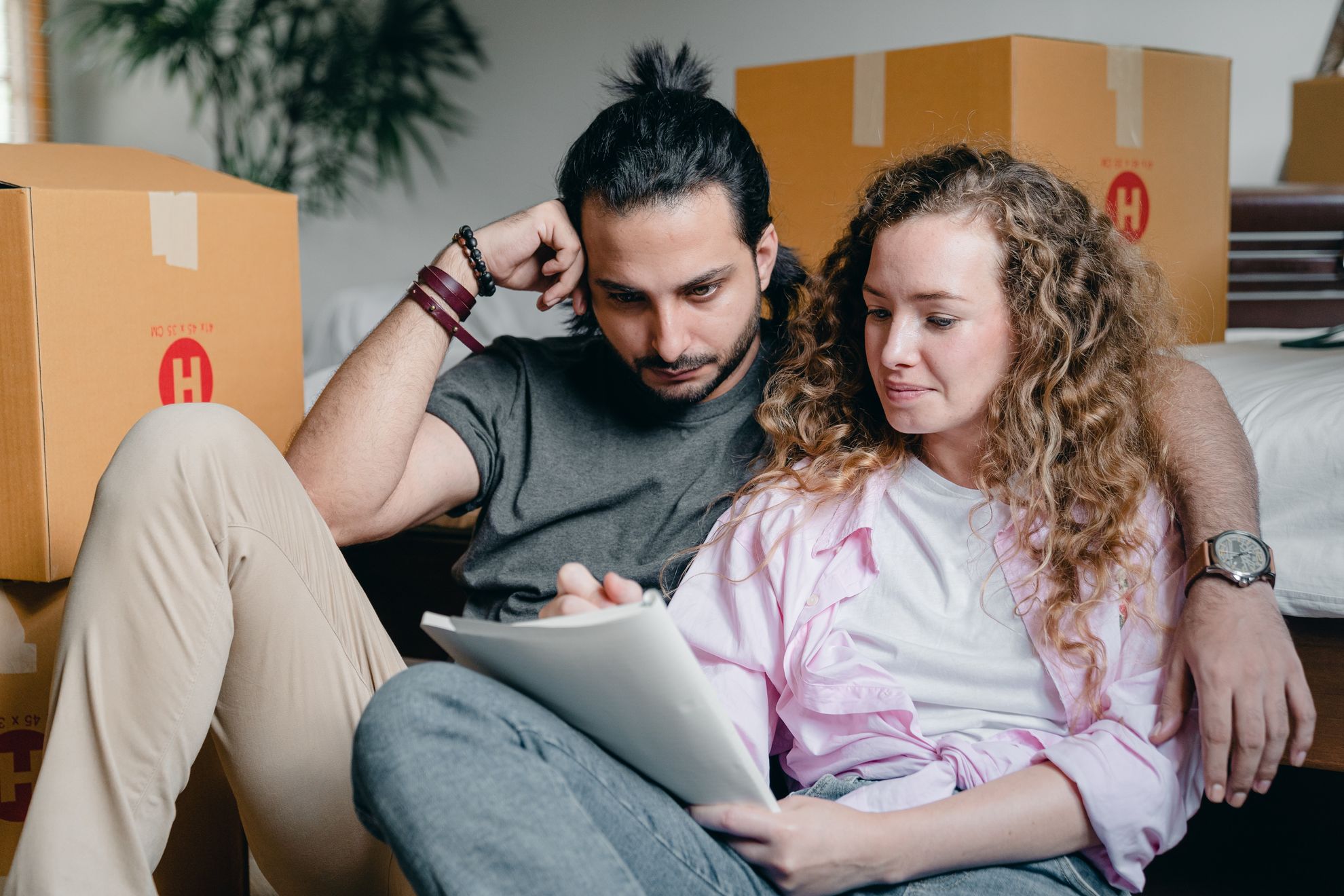 Man and woman sitting on a floor surrounded by cross-country moving boxes and with a piece of paper