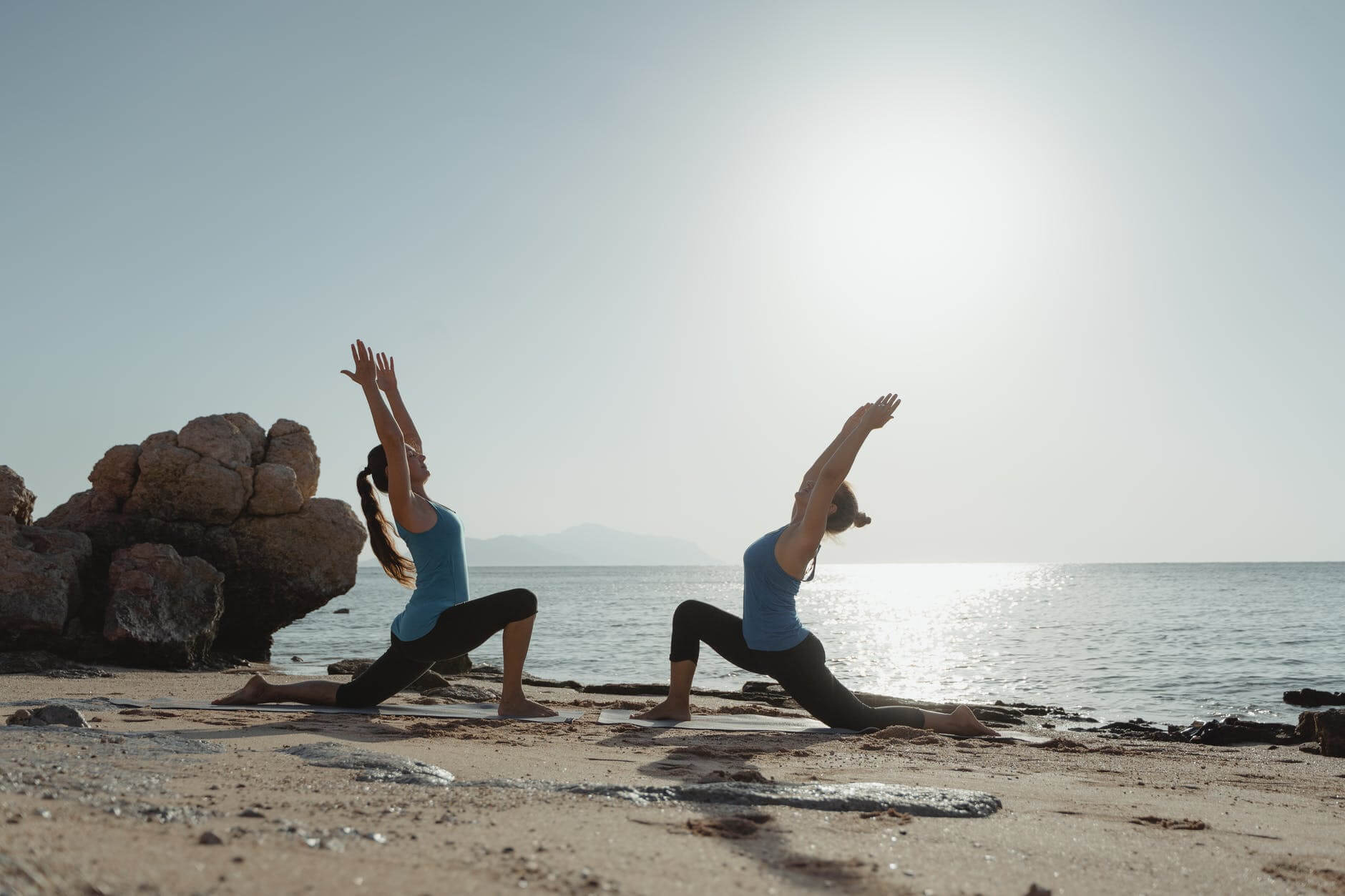 Two women exercising yoga on the beach