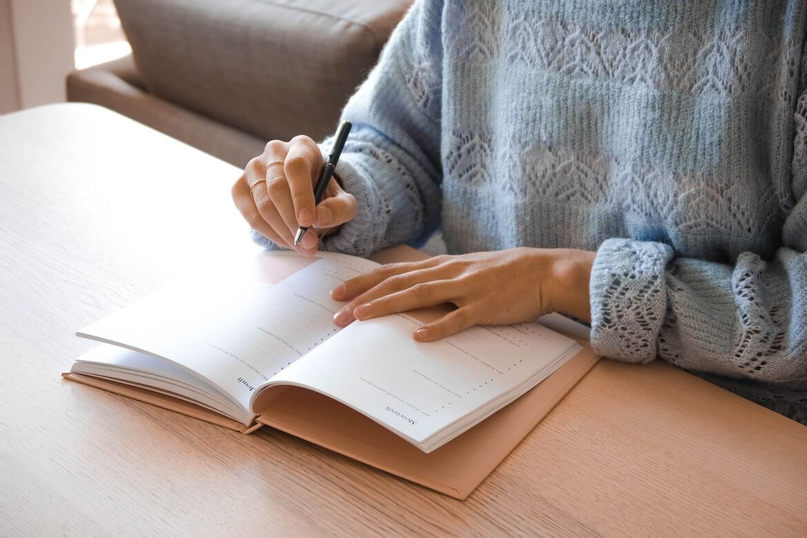 Woman in a gray sweater holding writing into a notebook