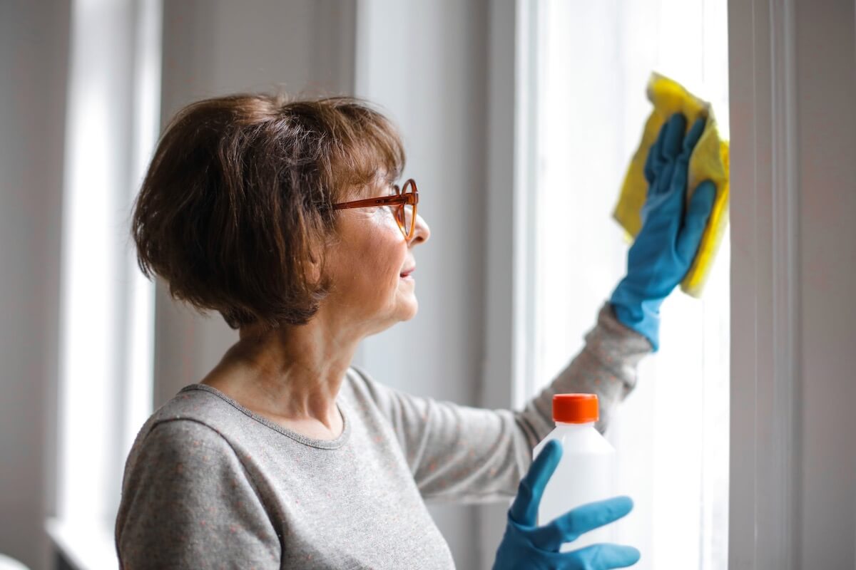 An older woman cleaning a window with gloves on