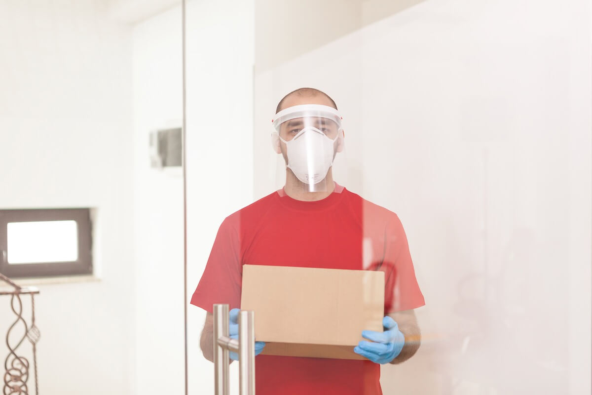 A mover in a red shirt with a mask on carrying a box