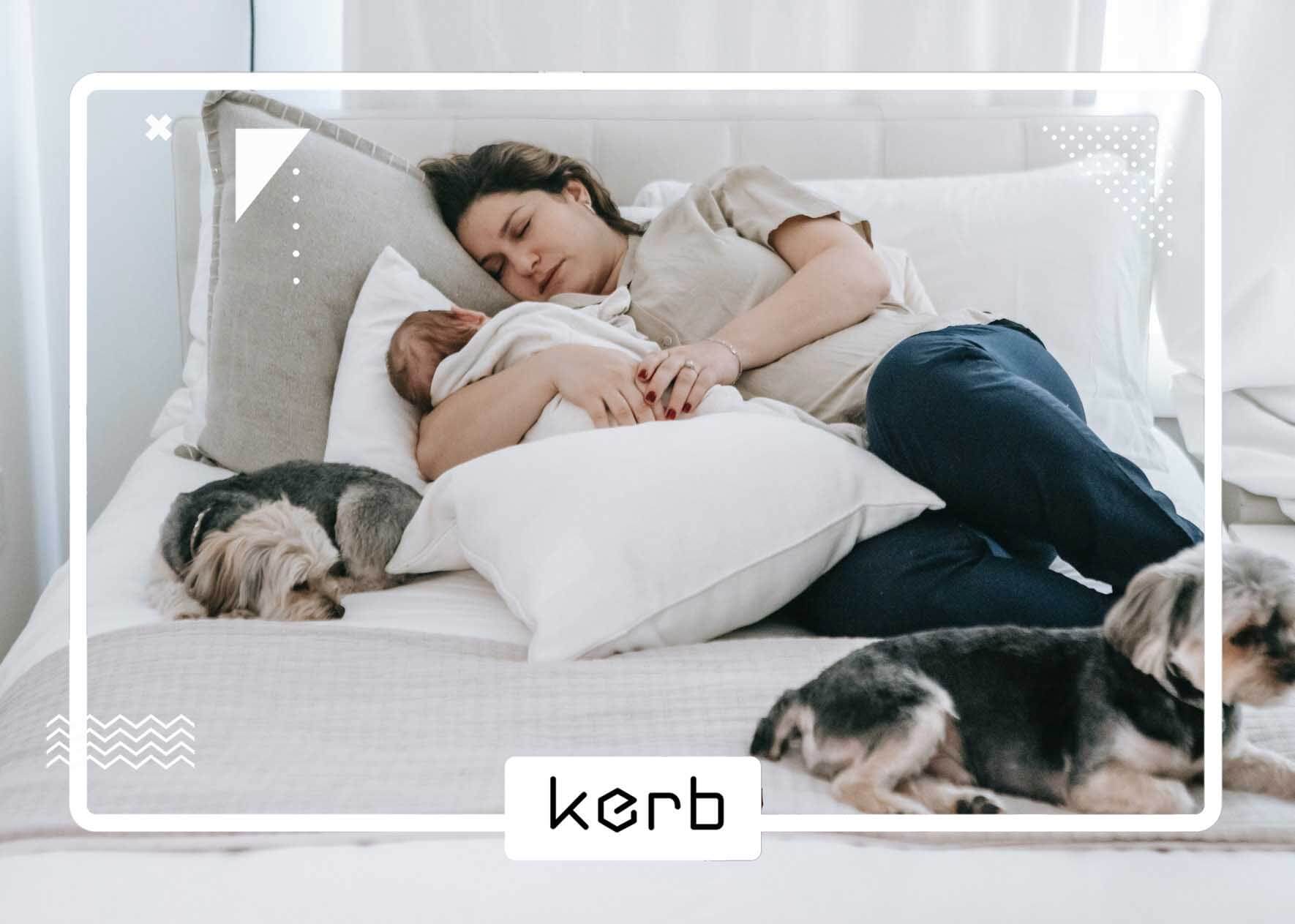 A mother, her baby, and two dogs lying on the bed