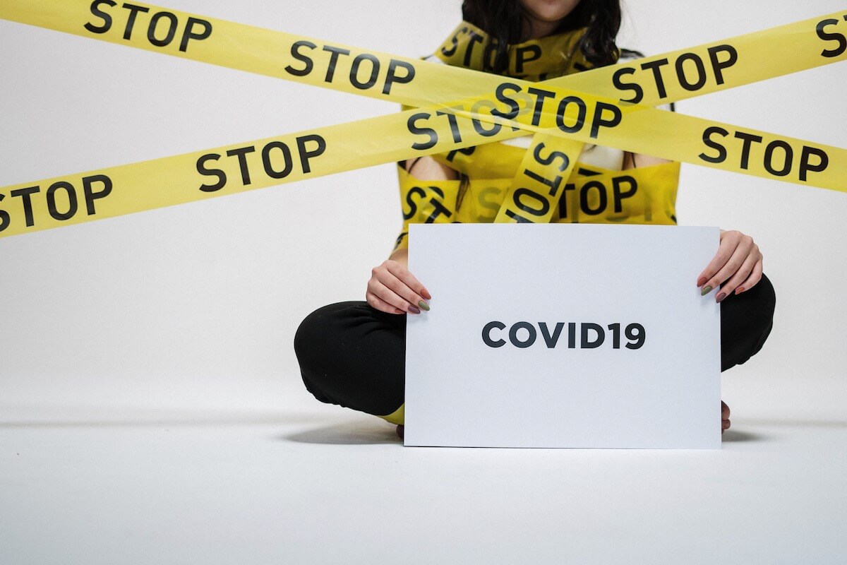 A woman holding a COVID-19 sign while being covered with tape