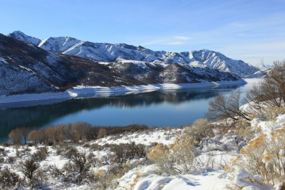 Large calm lake surrounded by majestic snow-covered mountains under a blue sky.